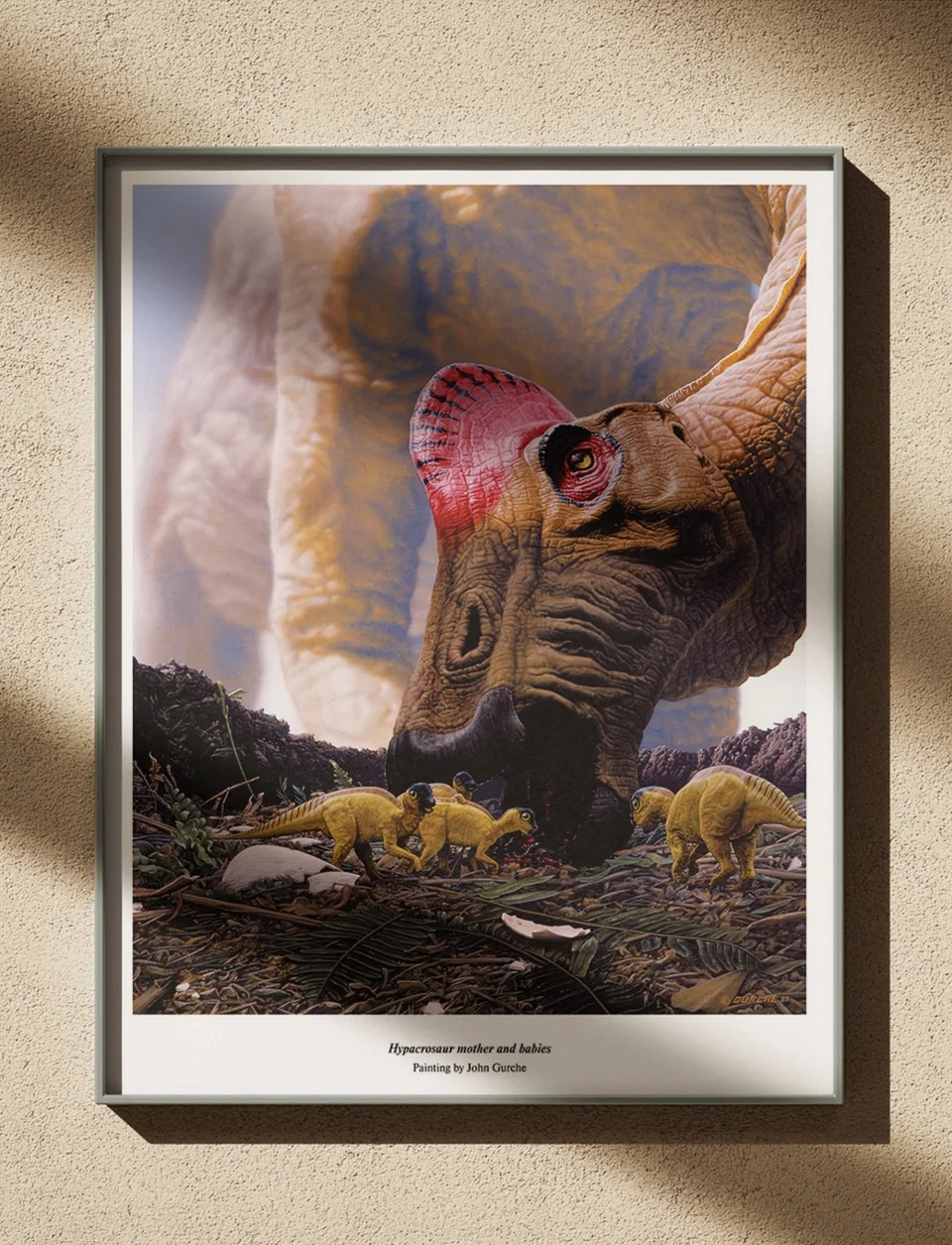 The Hypacrosaur mother and babies painting, framed in black on a warm plaster wall in low sun.