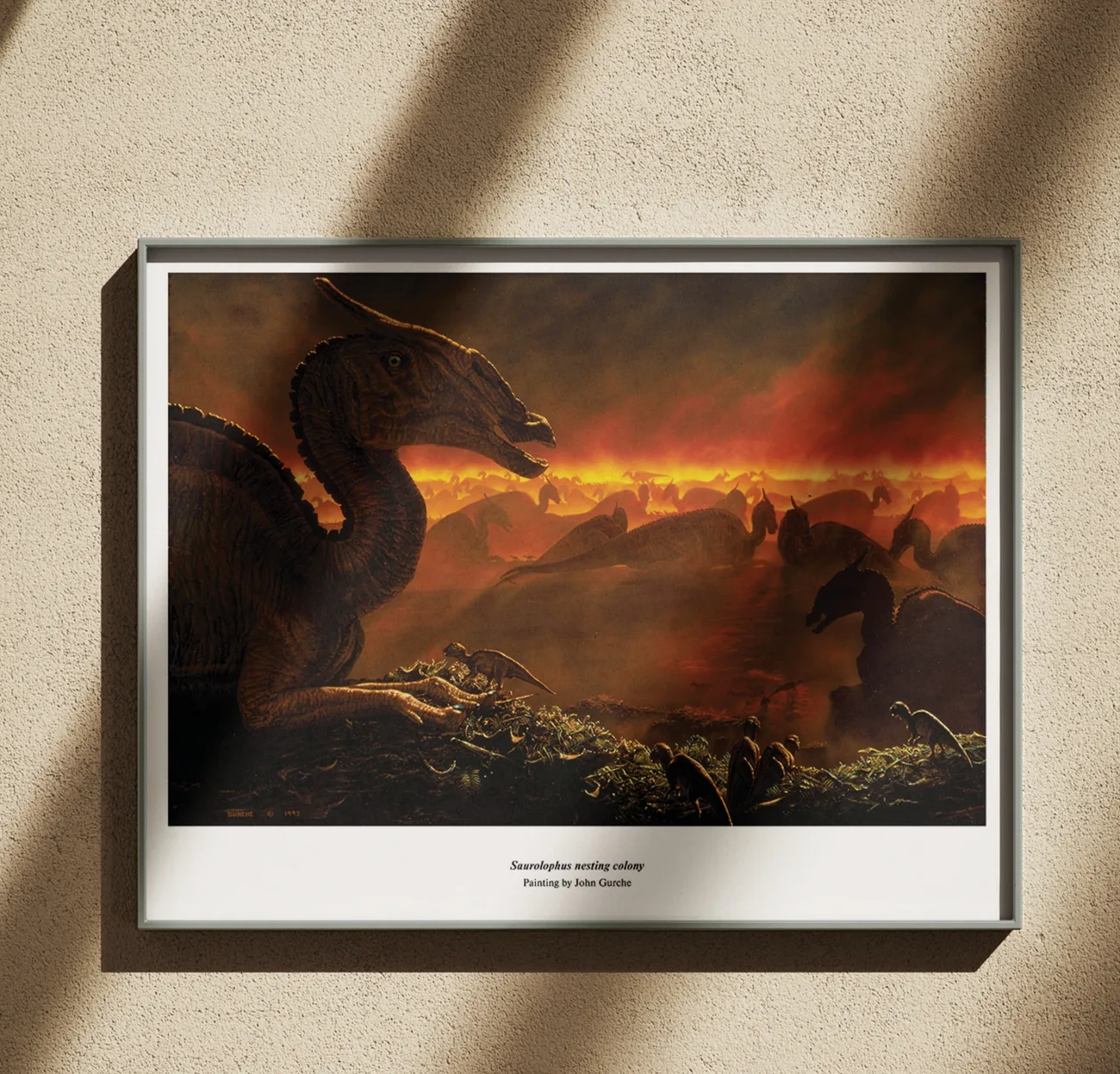 The Saurolophus nesting colony painting, framed in black on a warm plaster wall in raking sunlight.