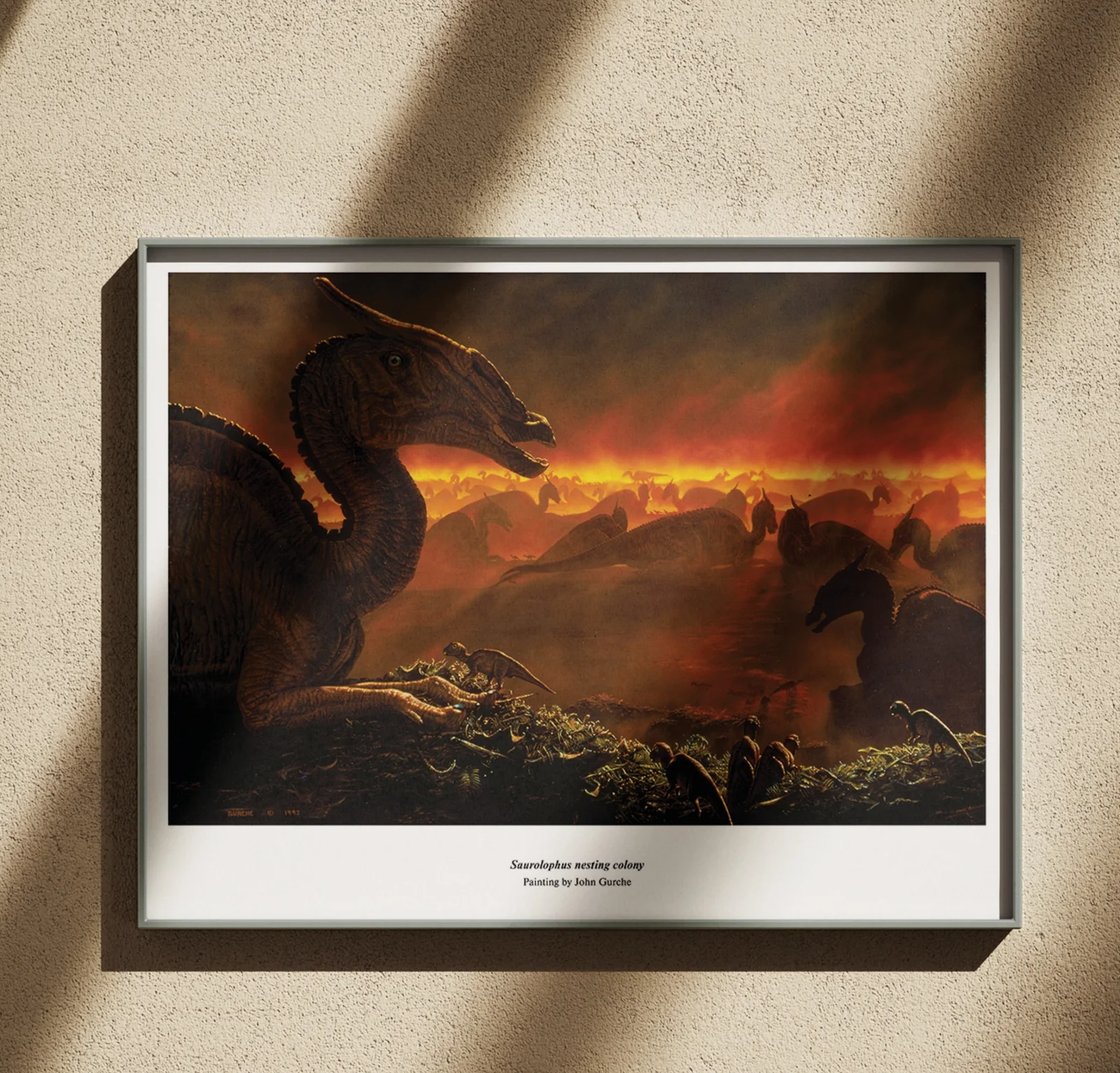 The Saurolophus nesting colony painting, framed in black on a warm plaster wall in raking sunlight.